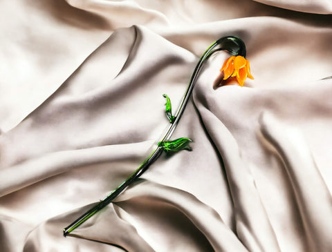 an orange flower is laying on a white sheet